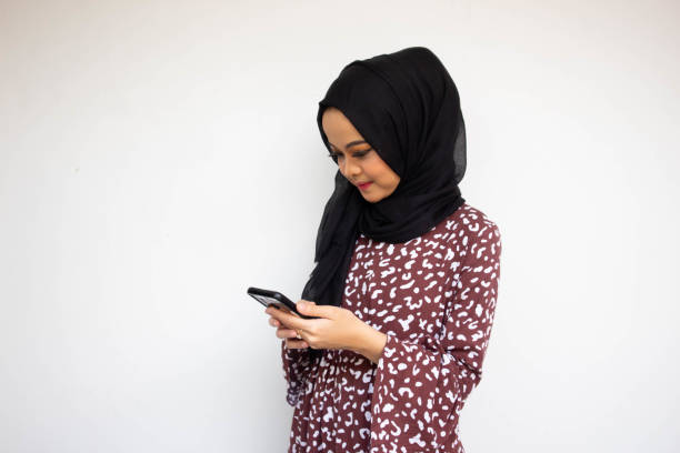 istock Asian hijab young woman isolated on white background smiling while using a cell phone 1438363271