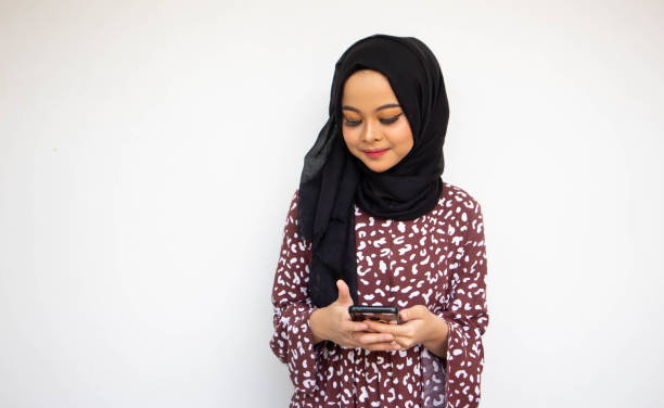 istock Asian hijab young woman isolated on white background smiling while using a cell phone 1438363282