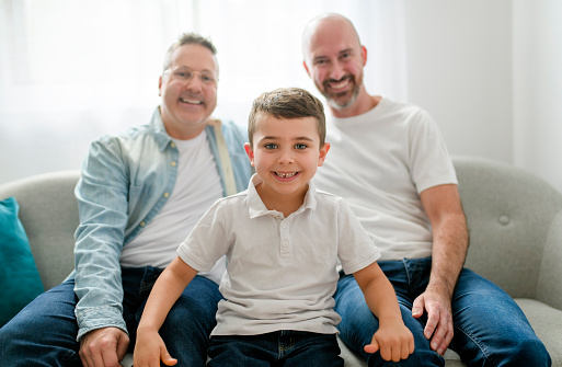 A Happytwo man couple with adopted child sit on sofa at home
