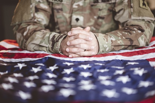An American soldier mourning and praying with the American flag in front of him