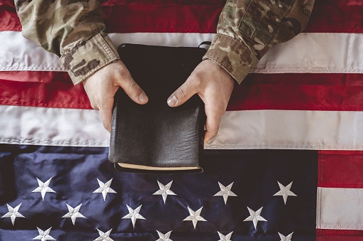 An American soldier mourning and praying with the Bible in his hands and the American flag