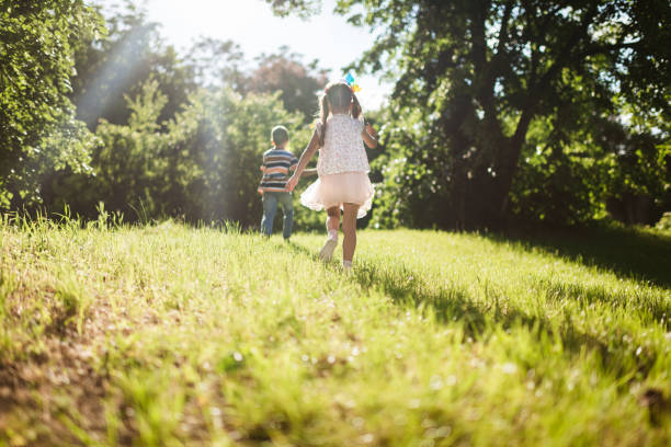 Beautiful smiling brother and sister running in nature on a sunset.