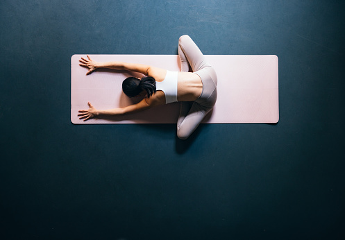 Directly above photo of an anonymous Asian woman in sportswear sitting on a exercise mat and stretching her arms and legs at yoga studio.
