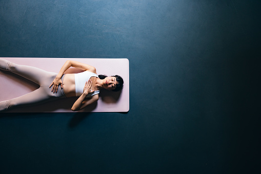 High angle view of serious Asian woman in sportswear lying down on a exercise mat at yoga studio.