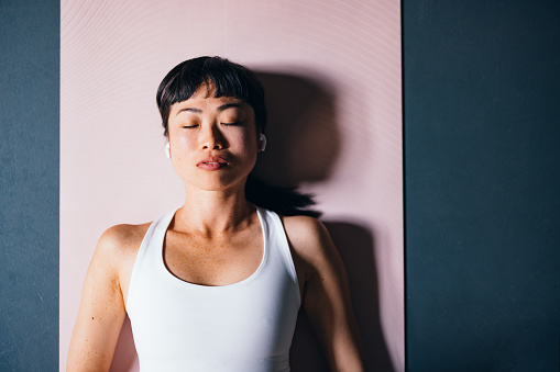 Directly above photo of serious Asian woman woman in sportswear listening to music on her wireless earphones before yoga session.