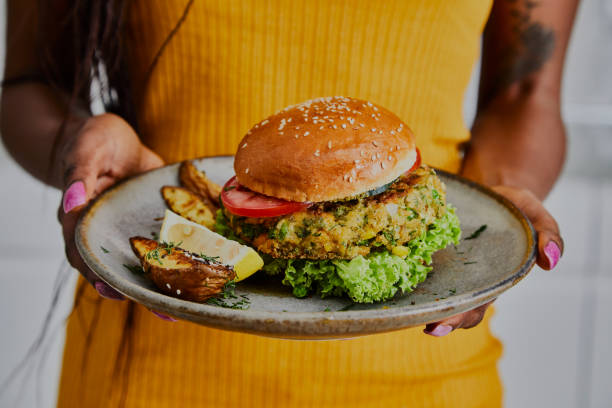 Beautiful and tasty vegan burger on a plate A woman holds a healthy vegan burger on a handmade ceramic plate, made of zucchini, green pea, seasoning, herbs and spices, close up vegan stock pictures, royalty-free photos & images