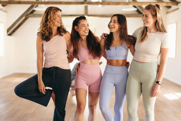Group of women standing together in a yoga studio Group of sporty women smiling happily while standing together in a yoga studio. Cheerful female friends working out together in a fitness studio. Women of different ages attending a yoga class. sports clothing stock pictures, royalty-free photos & images
