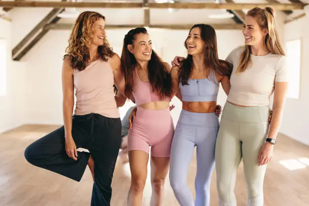 Group of sporty women smiling happily while standing together in a yoga studio. Cheerful female friends working out together in a fitness studio. Women of different ages attending a yoga class.