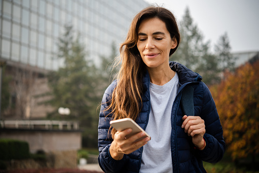 Portrait of a happy woman enjoying outdoors and using smartphone after work