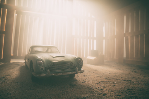 Beaconsfield, UK - November 1, 2022: An old and dusty Aston Martin DB5 sits neglected in an old wooden barn. Scale model photography.