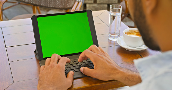 Over the shoulder view of man using laptop with green screen.