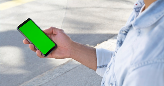 Close-up of man holding smartphone with green screen.