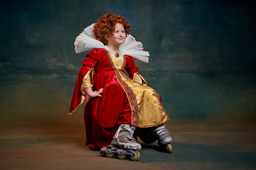 Portrait of little red-headed girl, child in costume of royal person in rollers isolated over dark green background. Concept of historical remake, comparison of eras, medieval fashion, emotions, queen