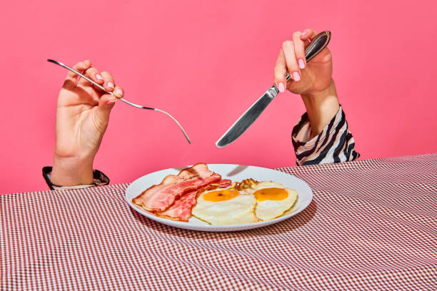 istock Female hands with fork and knife eating English breakfast with fried eggs and bacon 1438389360