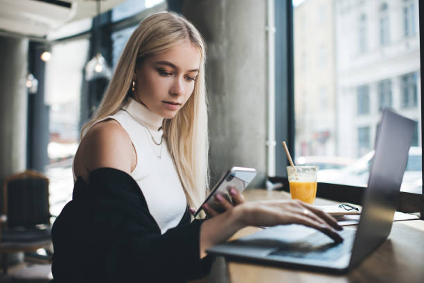 istock Elegant woman messaging on phone while using laptop in cafe 1438390138
