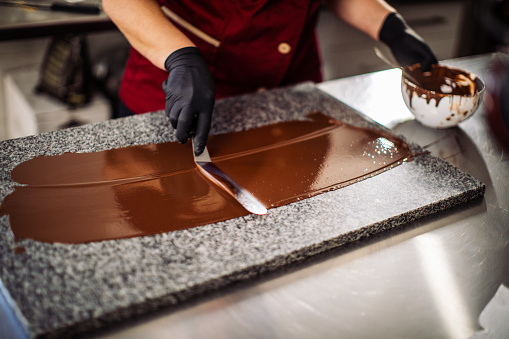 Mid adult woman making chocolate decorating elements for cake on icing stone table. She works in sweet food manufacture, small business company