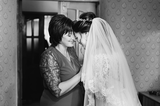 bride in white dress standing face to face with her mom on black and white photographs