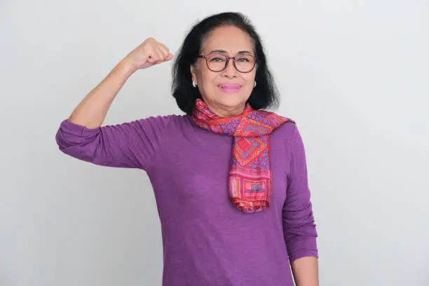 Asian elderly women smiling while showing her bicep muscle