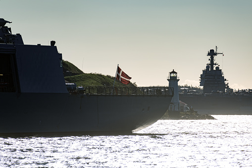 Navy ship enters a harbour after offshore training exercises. American aircraft carrier can be seen in the background.