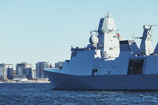 The frigate HMAS Arunta (right), destroyer HMAS Sydney (centre) and amphibious assault ship HMAS Canberra (left) of the Royal Australian Navy.  They are docked at Garden Island, Sydney Harbour, in preparation for an open day to the public during Navy Week, the first open day since the Covid pandemic.  A shadow from a skyscraper in the central business district is starting to make a shadow on the hull of HMAS Canberra.   This image was taken at sunset from Woolloomooloo Bay on 25 February 2023.