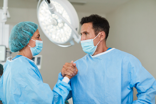 Surgeons congratulate each other after a successful outcome of a long and difficult medical procedure. Close-up waist up with copy space