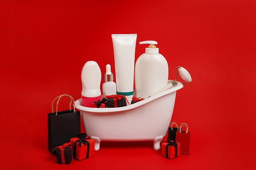 Bathtub with serum oil, beauty self care skin care mock up products and shopping bags, gift boxes on red background. black friday sale