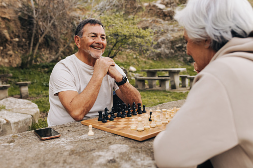 Carefree elderly couple playing a game of chess in a park. Happy senior couple spending some quality time together after retirement. Mature couple having a good time outdoors.