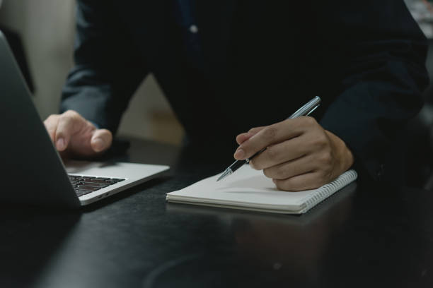 istock businessman hand holding pen writing on notebook working with laptop computer in modern office.Write on journal diary concept. 1438402283