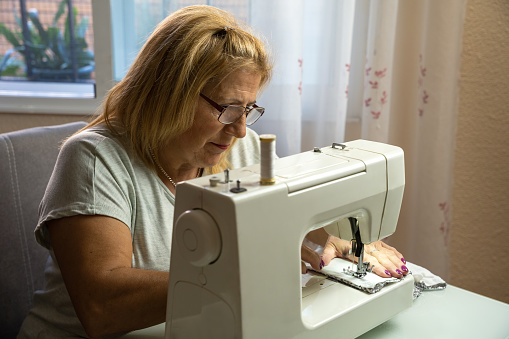 Woman seamstress with glasses concentrating while sewing at the sewing machine