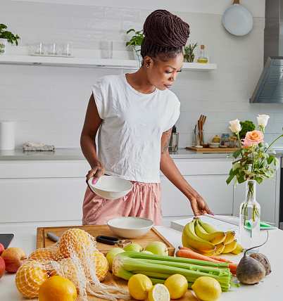 A beautiful black young adult woman in the kitchen, reading recipes, for healthy breakfast prepared at the kitchen table, representing healthy lifestyle, an image with a large copy space