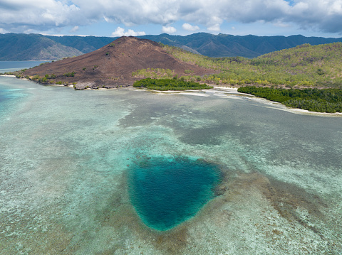 A fringing reef has a blue hole on the edge of a remote island near Alor, Indonesia. This region is known for its high marine biodiversity and spectacular scuba diving and snorkeling.