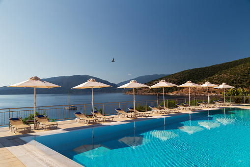 Luxury swimming pool with empty deck chairs and umbrellas at resort with beautiful sea view. Greek islands