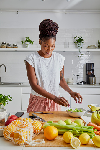 A young black adult woman in the kitchen, cutting fresh vegetables, fresh vegan or vegetarian food preparation at the kitchen table, representing healthy lifestyle, an image with a large copy space