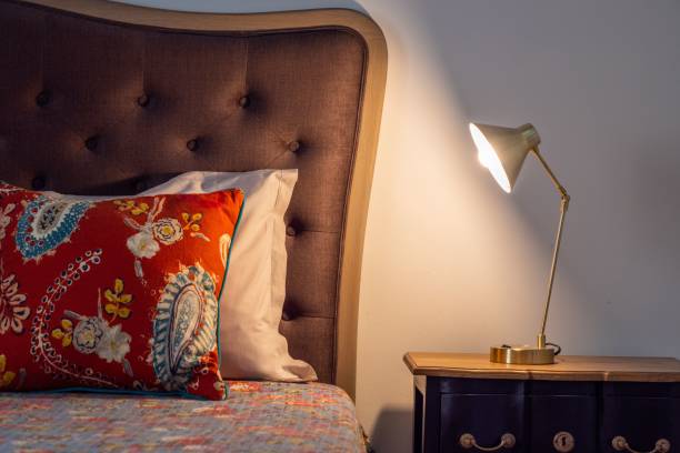 istock Vintage bed corner with a brown headboard, antique style pillows, and a bedside table with a lamp 1438407400