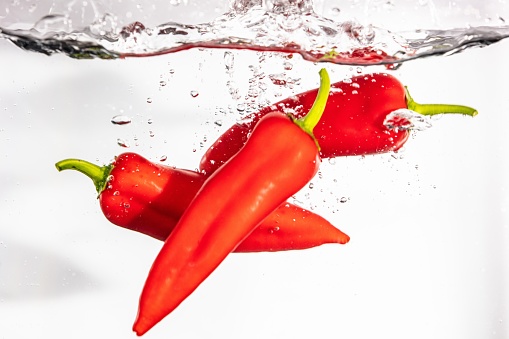 A closeup shot of three red tabasco peppers in the water on a white background