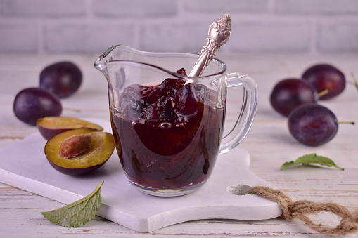 Plum jam in a glass gravy boat on a white wooden background.