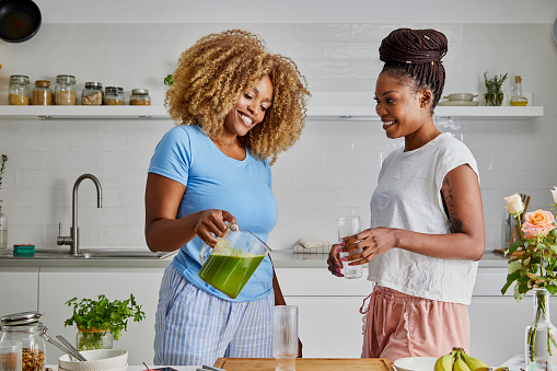 A beautiful black young adult women in a modern kitchen, fresh vegan or vegetarian food preparation at the kitchen table, representing healthy lifestyle, an image with a copy space