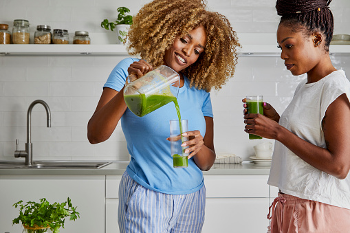 A beautiful black young adult women in the kitchen, fresh vegan or vegetarian food preparation at the kitchen table, fresh organic juice drinking for breakfast, representing healthy lifestyle, an image with a copy space