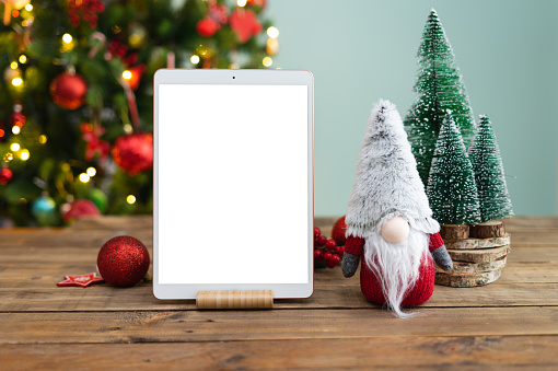 Tablet in vertical with blank screen for mockup. Wooden table with tablet and Christmas decoration. Tablet upright on stand for mockup.