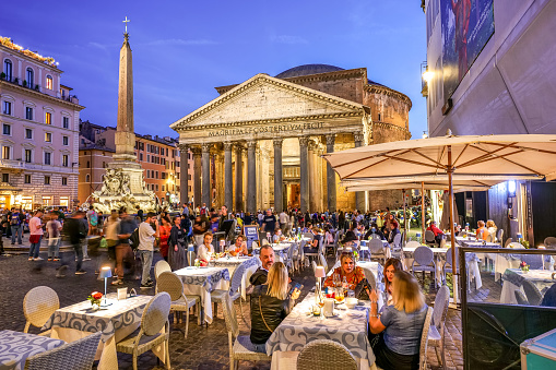 Rome, Italy, 01 November -- A suggestive evening view of the Roman Pantheon and Piazza della Rotonda in the heart of the Eternal City, with dozens of tourists sitting among the outdoor tables of typical Italian restaurants. Built in 27 BC by the Consul Marco Vispanio Agrippa for the emperor Augustus and dedicated to the Roman divinities, the majestic Pantheon is one of the best preserved Roman structures in the world. The fountain with the Egyptian obelisk in the center of the square was built by the sculptor Leonardo Sormani in 1575 on a project by the architect Giacomo della Porta. In 1980 the historic center of Rome was declared a World Heritage Site by Unesco. Super wide angle image in high definition format.