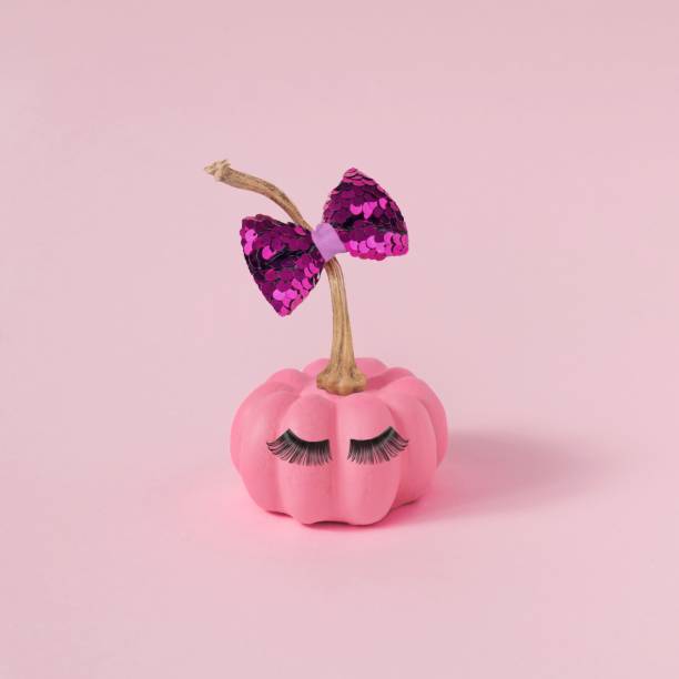 istock Halloween pink pumpkin with makeup, false eyelashes, and a bow tie on the pink background, close-up 1438413194
