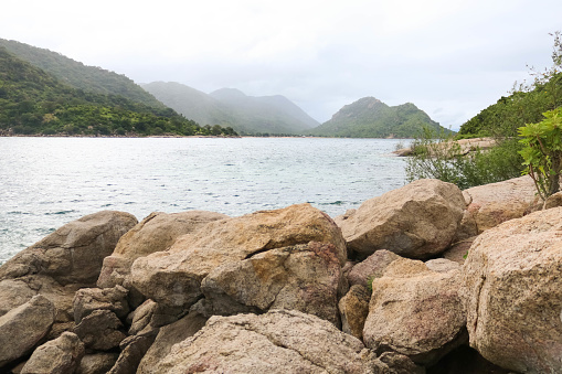 The sea surrounded by rocks and hills covered in greenery under a cloudy sky