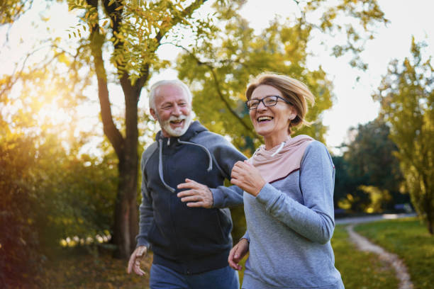 веселая активная пожилая пара бегает трусцой в парке - senior adult running jogging senior women стоковые фото и изображения