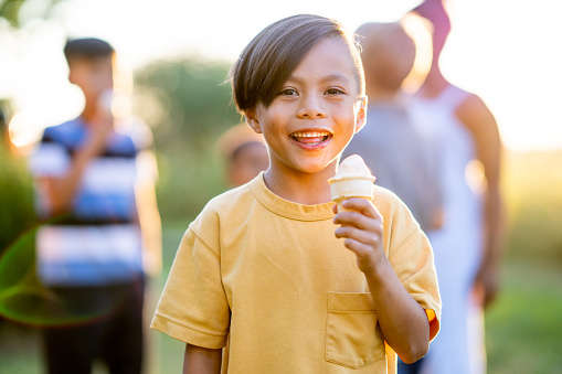 An adorable child smiles for the camera while standing with his ice cream cone in hand.