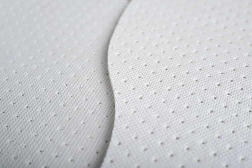 Textured surface of white hygienic shoe insoles with holes for ventilation. Close-up, low angle view, selective soft focus.