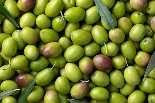 Fresh raw green olives and leaves close up full frame as background