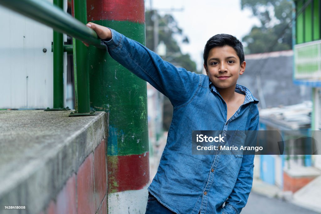 latin boy with an average age of 10 years old is on the street looking at the camera that portrays him while smiling Latino boy of average age of 10 years casually dressed in a jeans shirt stands in the street of his neighborhood looking at the camera that portrays him while smiling Adolescence Stock Photo