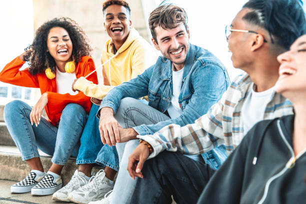 College students having sun sitting in university campus - Multiracial young people talking and laughing together hanging outside in the city - Friendship concept with guys and girls enjoying day out stock photo