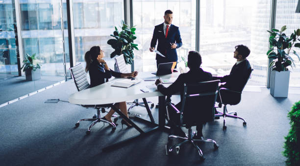 istock Caucasian corporate boss explaining information during training conference meeting with male and female employees, experienced businessman dressed in formal suit holding paper financial report 1438421950