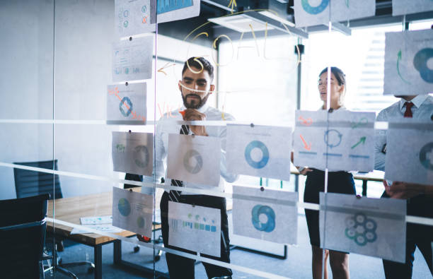 istock Diverse team developing plan and goals by writing and sticking papers on glass wall 1438422144